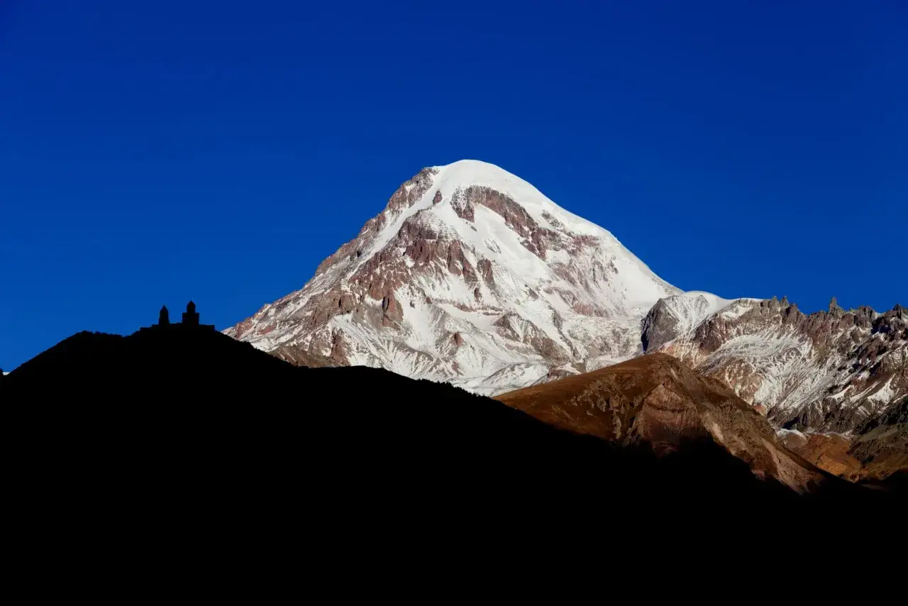 Majestatyczny Kazbek w Gruzji, ośnieżony szczyt góruje nad sylwetką cerkwi Gergeti.