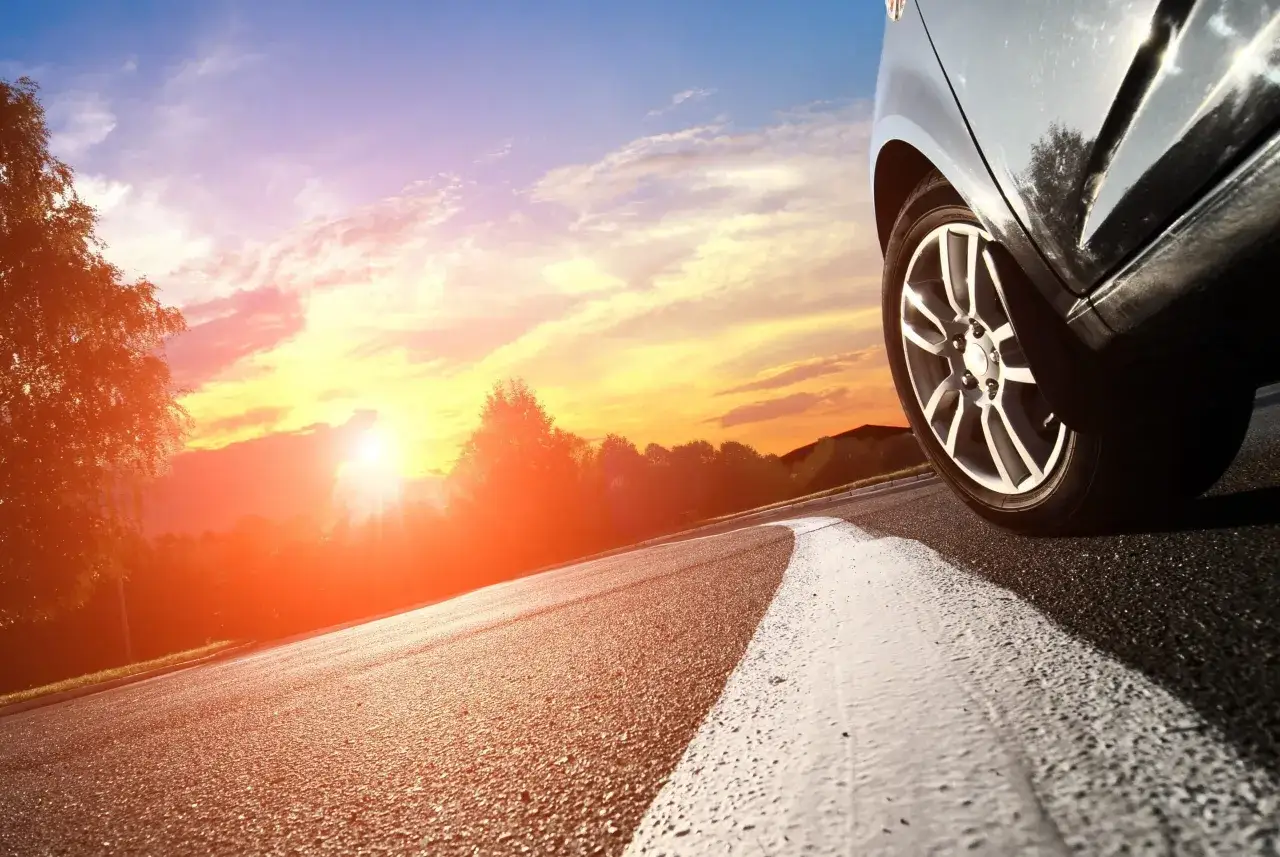 Un pneu de voiture sur une route au coucher du soleil, le soleil rasant illumine le ciel de couleurs chaudes.