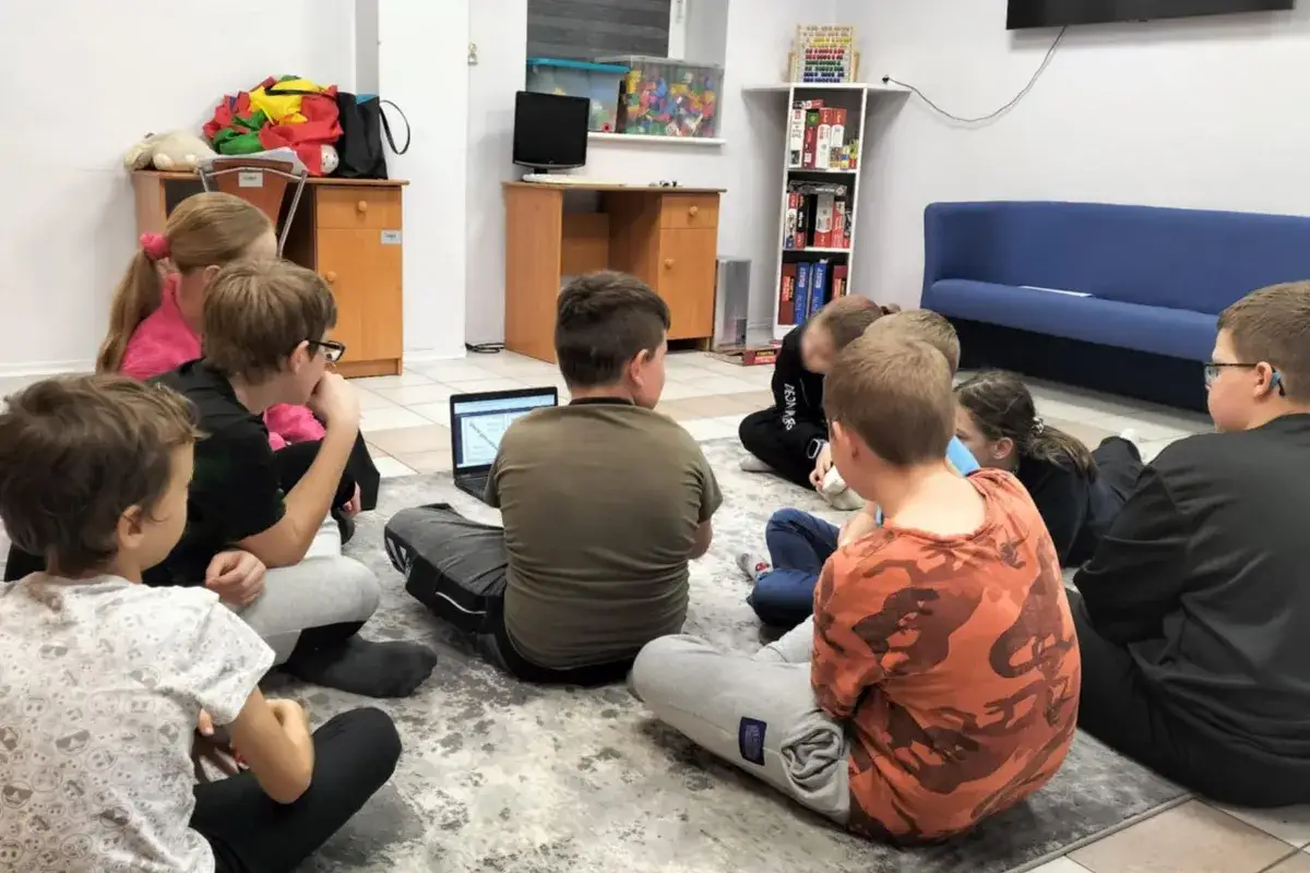 Dzieci uczą się o etapach rozwoju dziecka tabela, siedząc na dywanie przed laptopem.