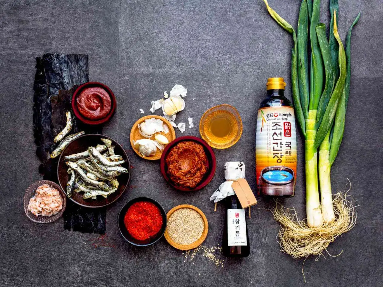 En samling koreanska basvaror att ha hemma: torkad fisk, vitlök, gochujang, sesamolja, chilipulver, sesamfrön, salladslök och sojasås.