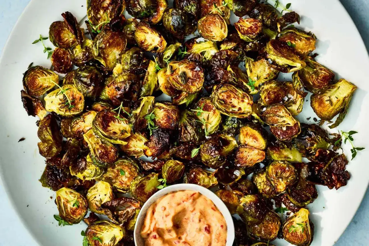 Knusprig gebratenen Rosenkohl mit Kräutern und einer cremigen Dip-Sauce auf einem Teller.