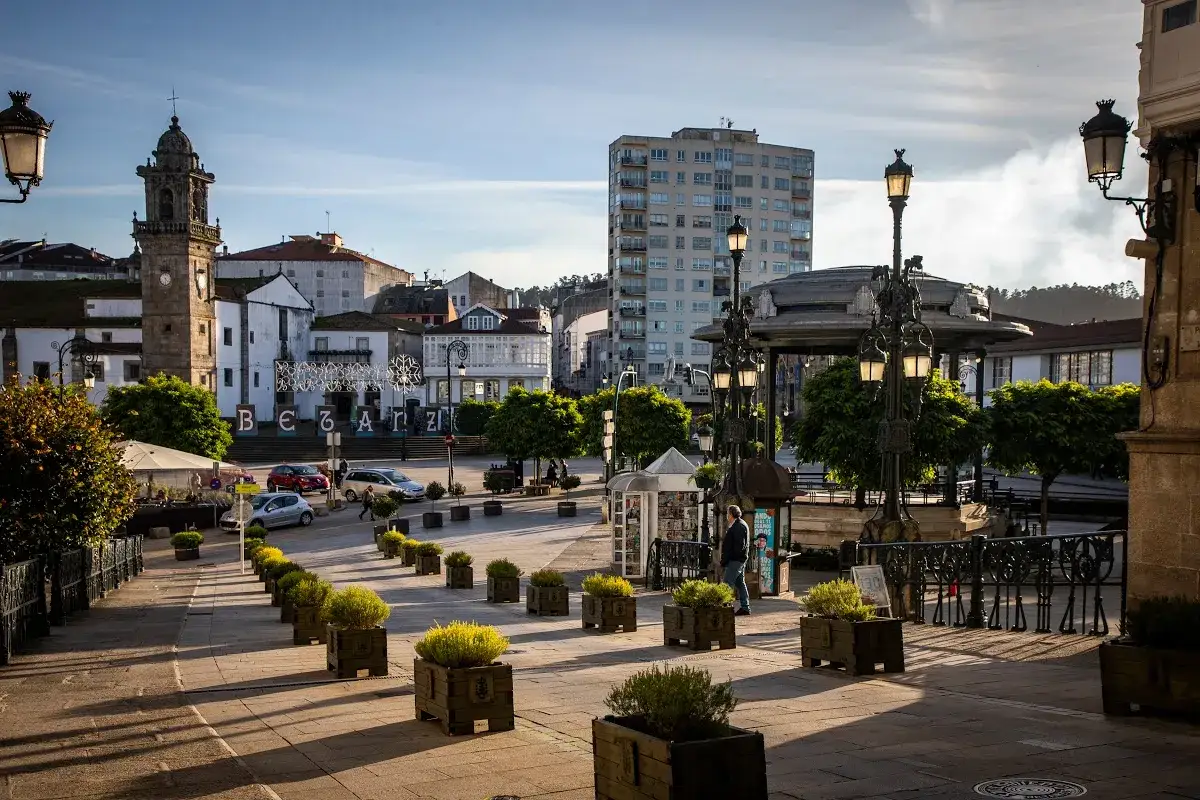 La plaza Betanzos, con su torre campanario y edificios hist&oacute;ricos, se ilumina con el sol de la tarde.