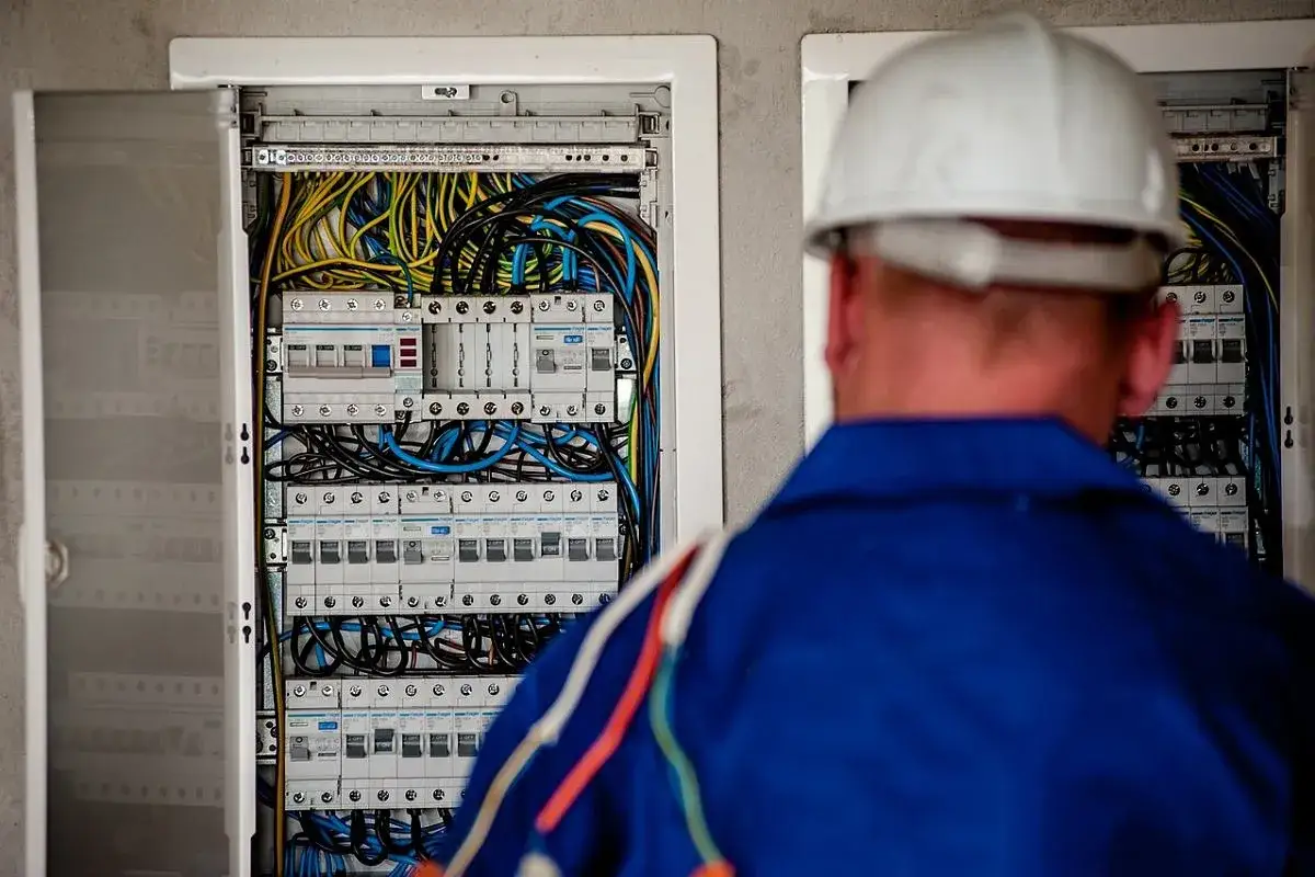 Elektryk w białym kasku przy skrzynce z bezpiecznikami. Zastanawiasz się, ile zarabia technik elektronik?