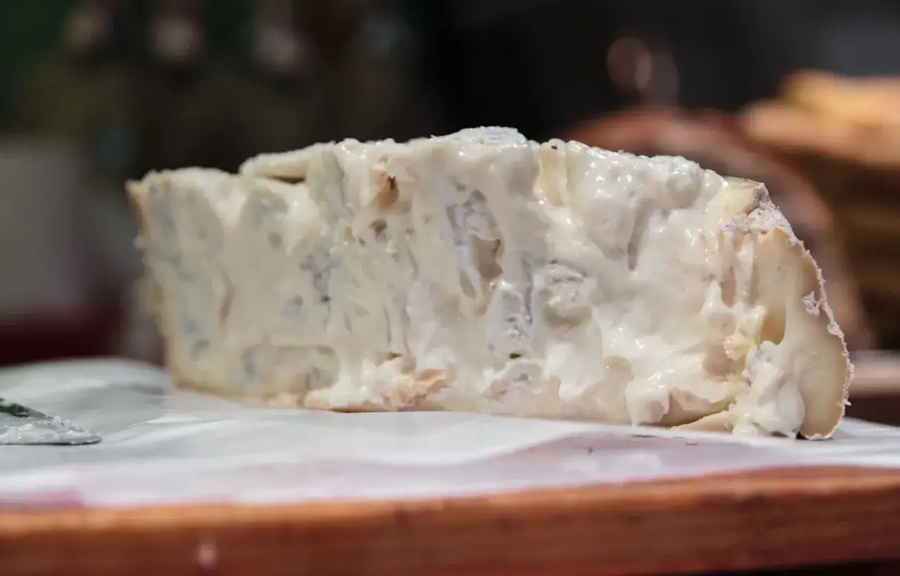 Un trozo cremoso de gorgonzola que es un queso azul italiano, con vetas azules y blancas, sobre papel blanco.