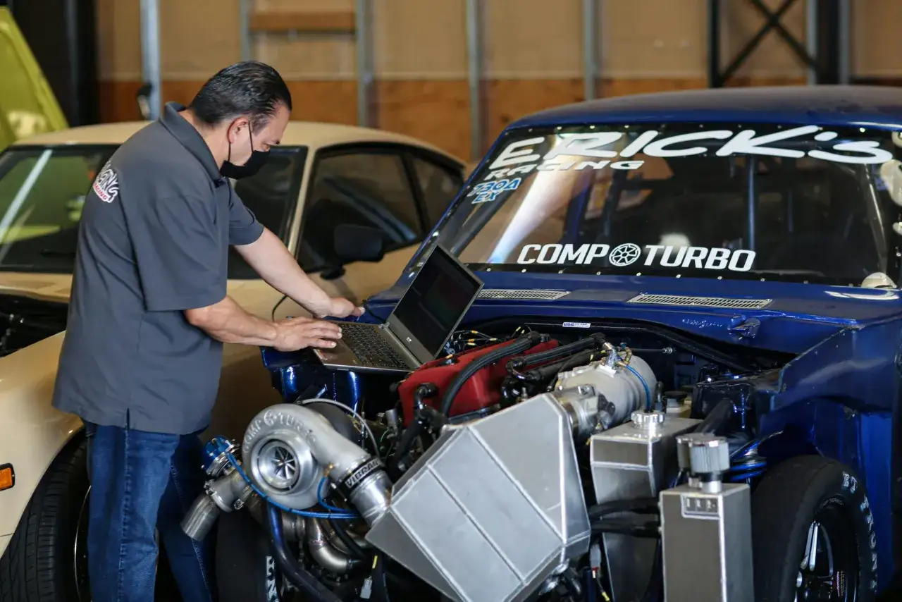 Mec&aacute;nico ajusta un coche de carreras azul con turbo para aumentar potencia, usando una laptop para la calibraci&oacute;n.