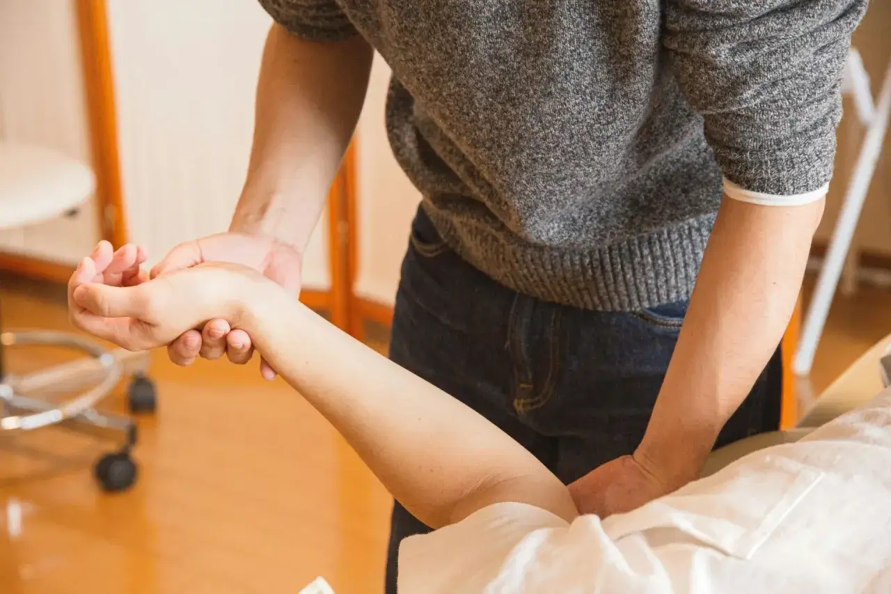 Fizjoterapeuta delikatnie masuje rękę pacjentki, kt&oacute;ra po zdjęciu gipsu jest jeszcze trochę krzywa.