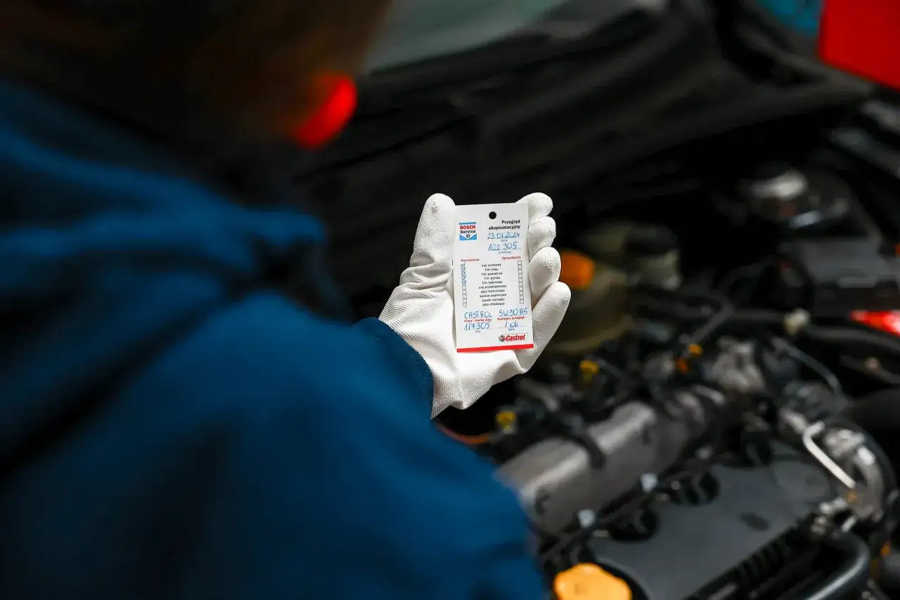 Mechanik w białej rękawiczce pokazuje karteczkę z informacją o wymianie oleju Castrol 5W30 A5, kluczowe dla silnika diesla.