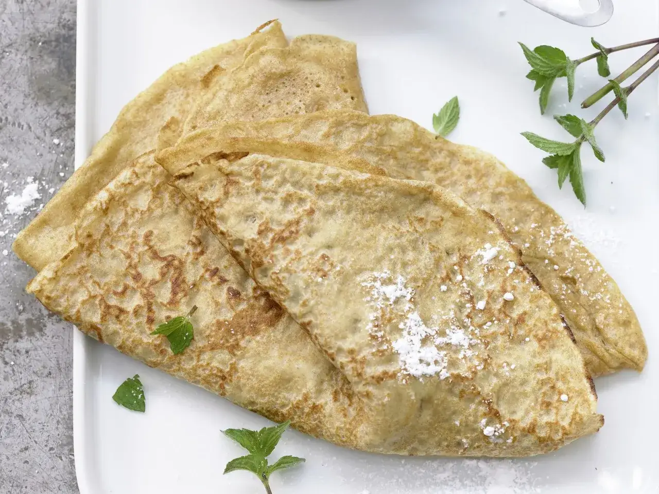 Drei goldbraune Dinkel Pfannkuchen, leicht mit Puderzucker bestäubt und mit frischer Minze garniert, warten auf das Dinkel Pfannkuchen Rezept.