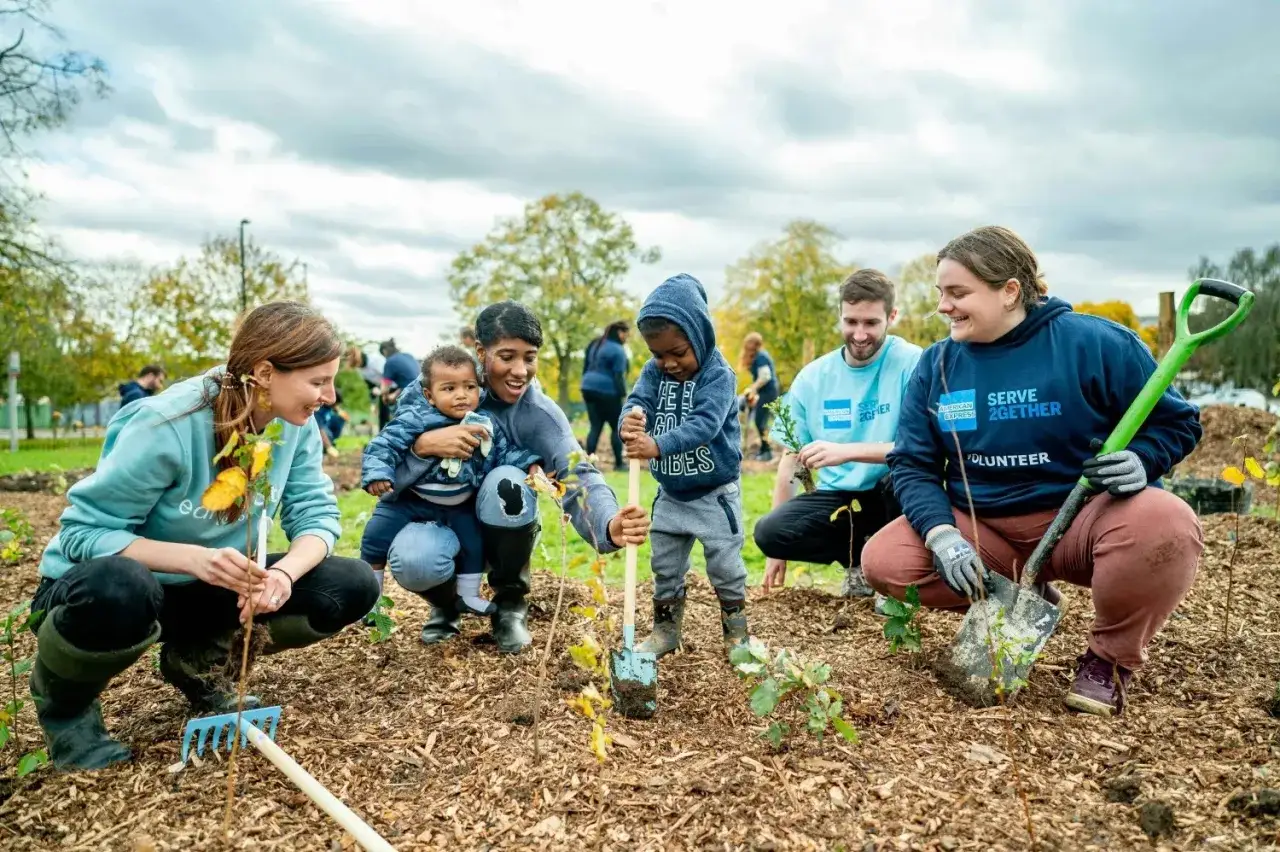 Volunteers plant trees, a great way to learn how to start a volunteer program. Families and children participate in this community gardening event.