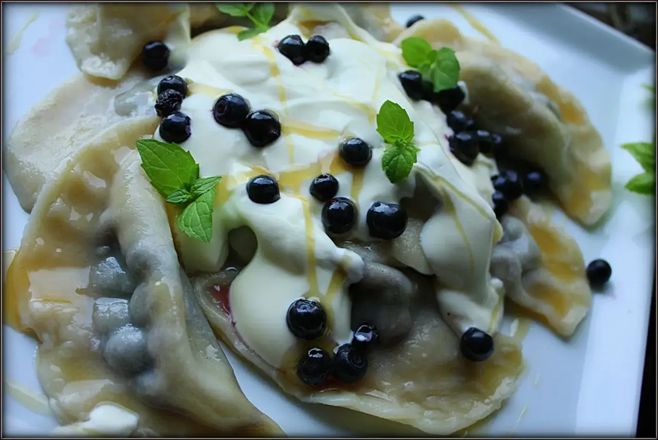 Pyszne pierogi z jagodami, polane śmietaną i miodem, ozdobione listkami mięty.