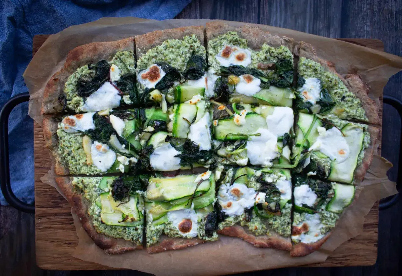 Geschnittene Pizza mit grünem Pesto, Zucchini, Spinat und Mozzarella auf einem protein pizza teig.