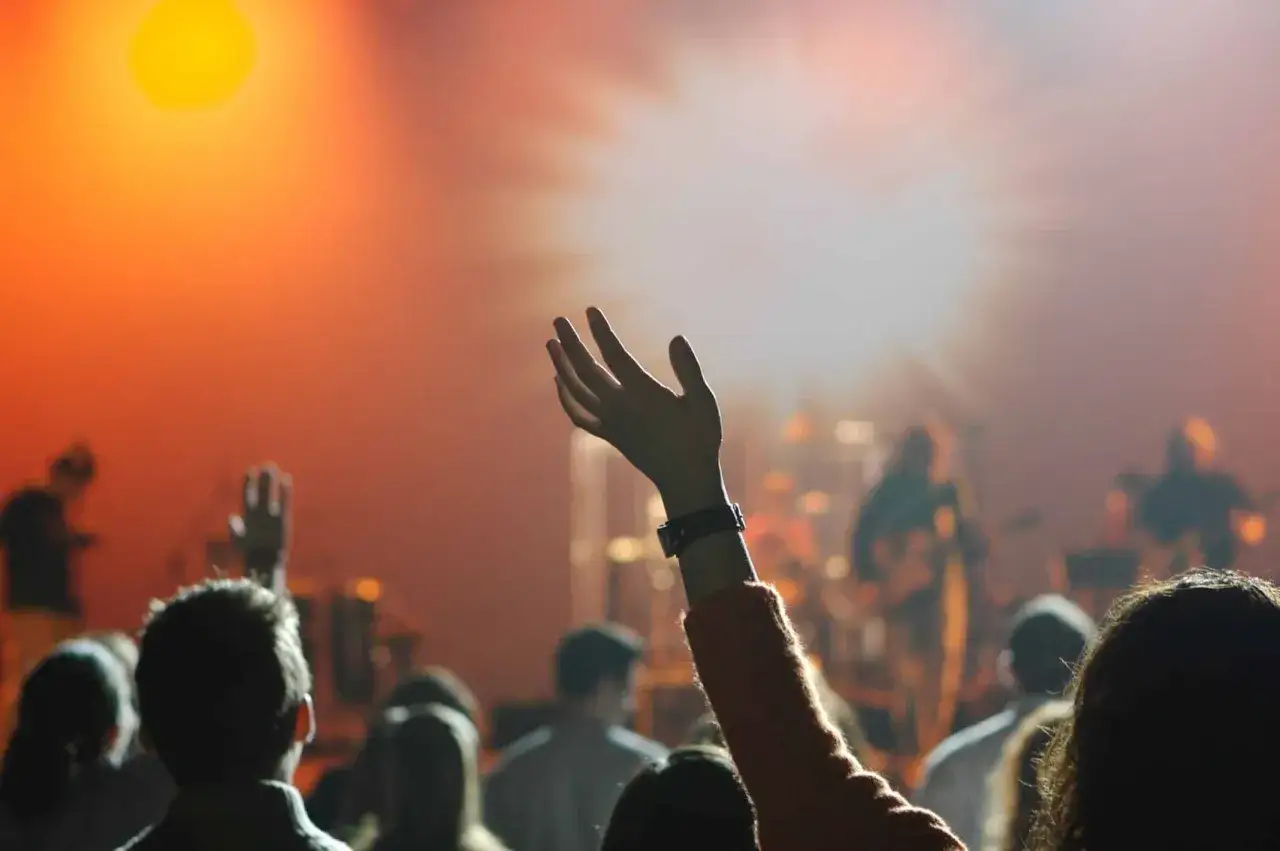 Menschen heben im Scheinwerferlicht die H&auml;nde. Eine Hand ragt empor, als Zeichen der Hingabe in der new life church.