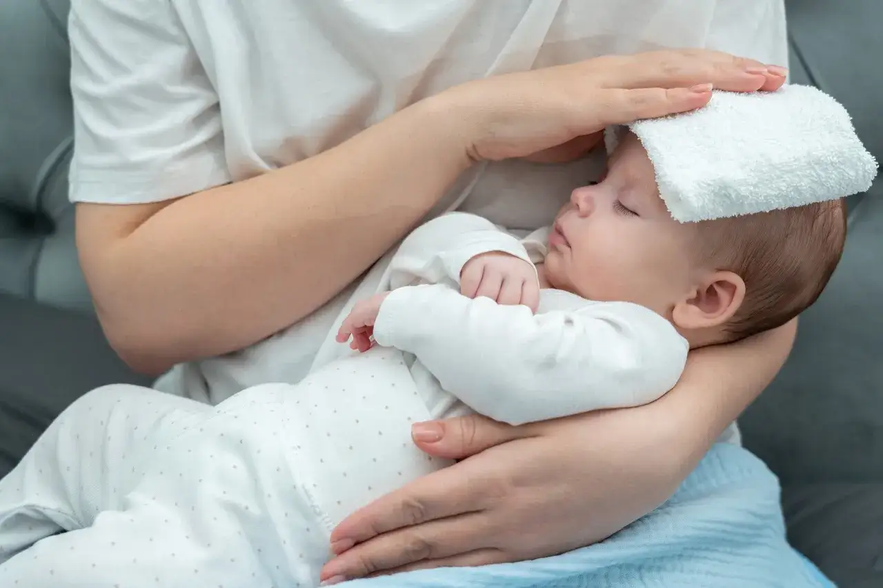 Beb&eacute; con pa&ntilde;o fr&iacute;o en la frente, cuidando s&iacute;ntomas de covid en beb&eacute;s.