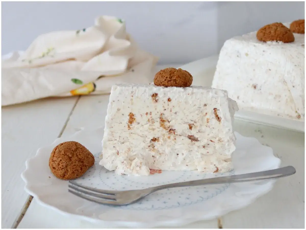 Una fetta di semifreddo agli amaretti, decorata con un amaretto intero, su un piatto bianco.