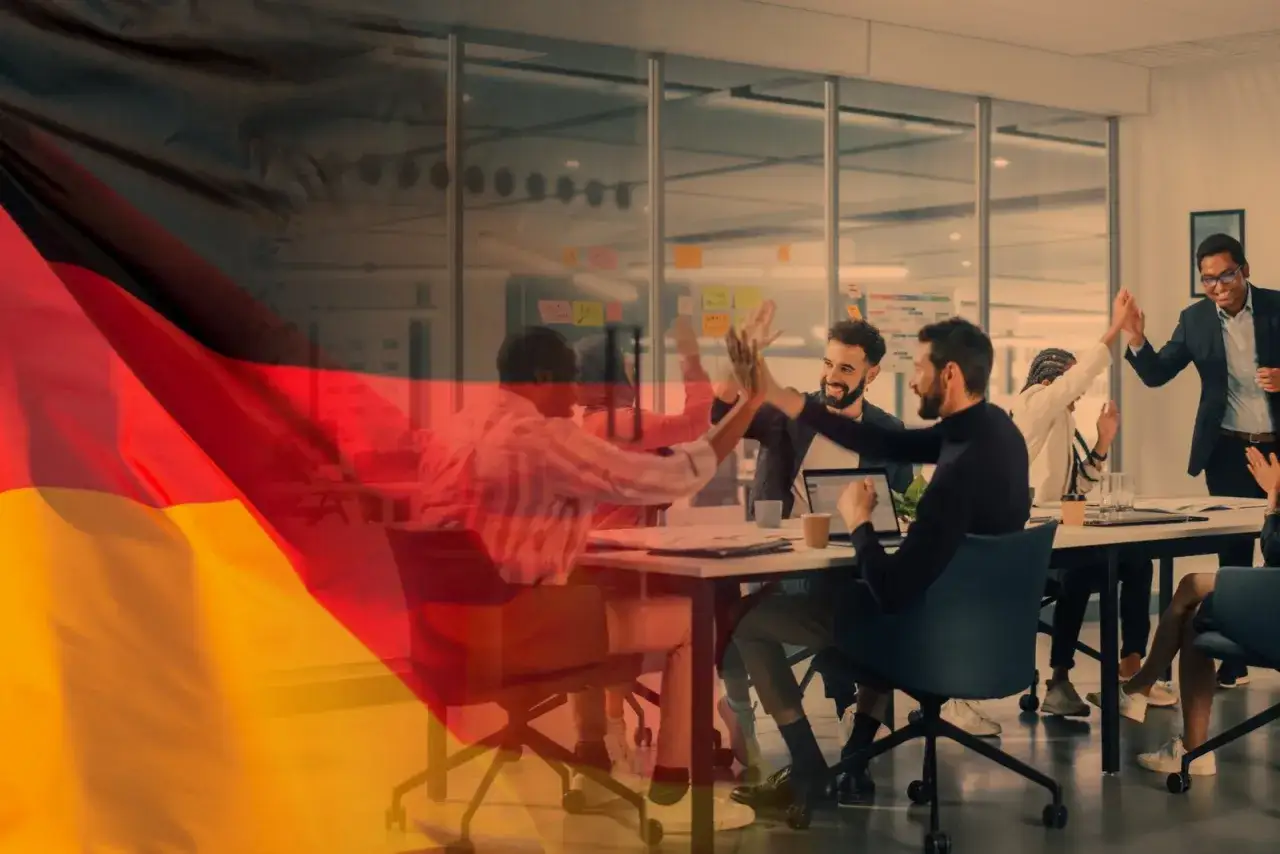 Team di successo celebra in ufficio, con la bandiera tedesca sovrapposta. Opportunità di offerte di lavoro in Germania senza lingua tedesca.
