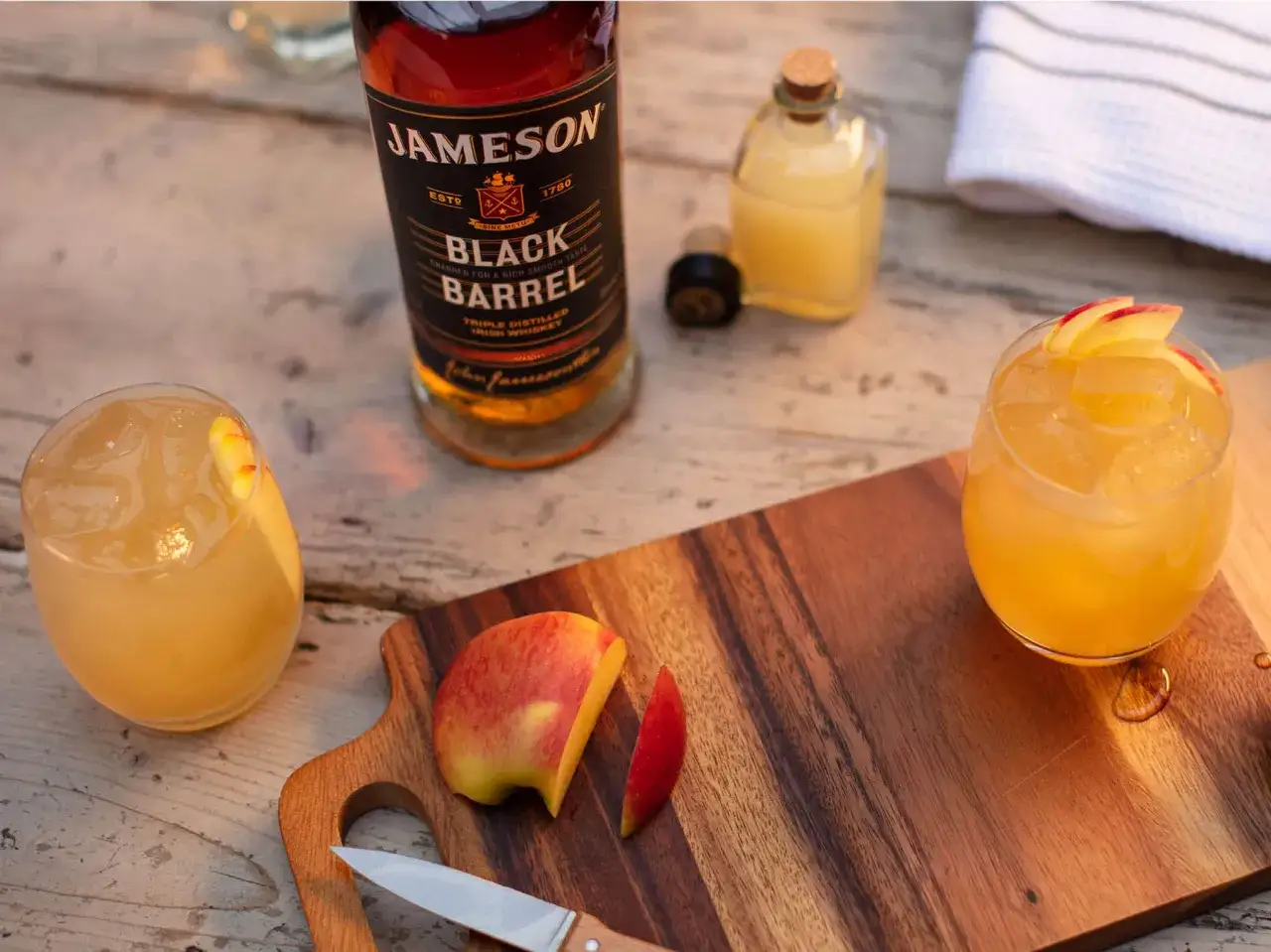 Orzeźwiający drink: whisky Jameson Black Barrel z sokiem jabłkowym, ozdobiony plasterkami jabłka. Idealny na letnie popołudnie.