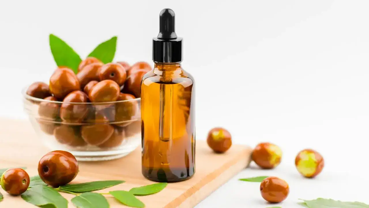 Aceite de jojoba, con sus maravillosas propiedades, en un frasco ámbar junto a frutos y hojas.