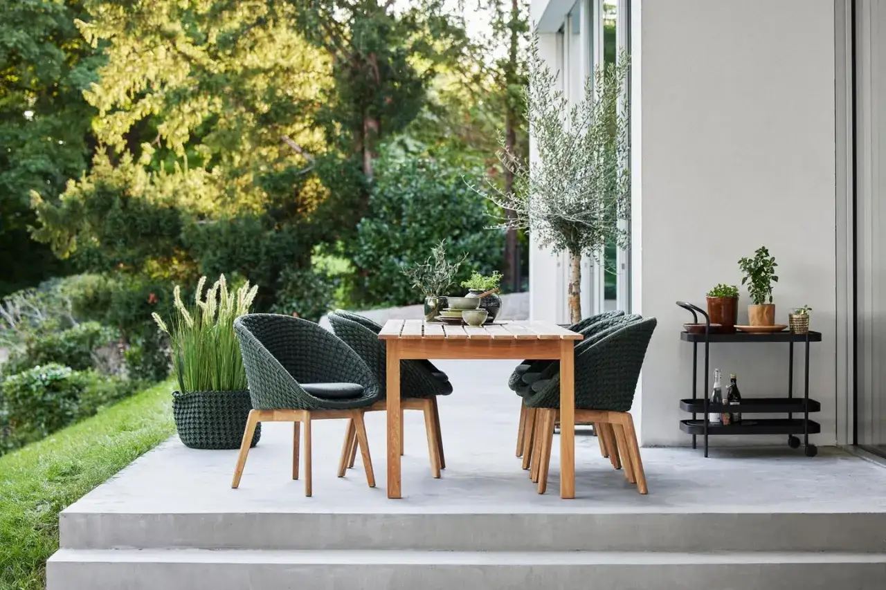 Gem&uuml;tliche Terrasse mit Holztisch, geflochtenen St&uuml;hlen und Pflanzen &ndash; tolle garten ideen f&uuml;r entspannte Stunden im Freien.