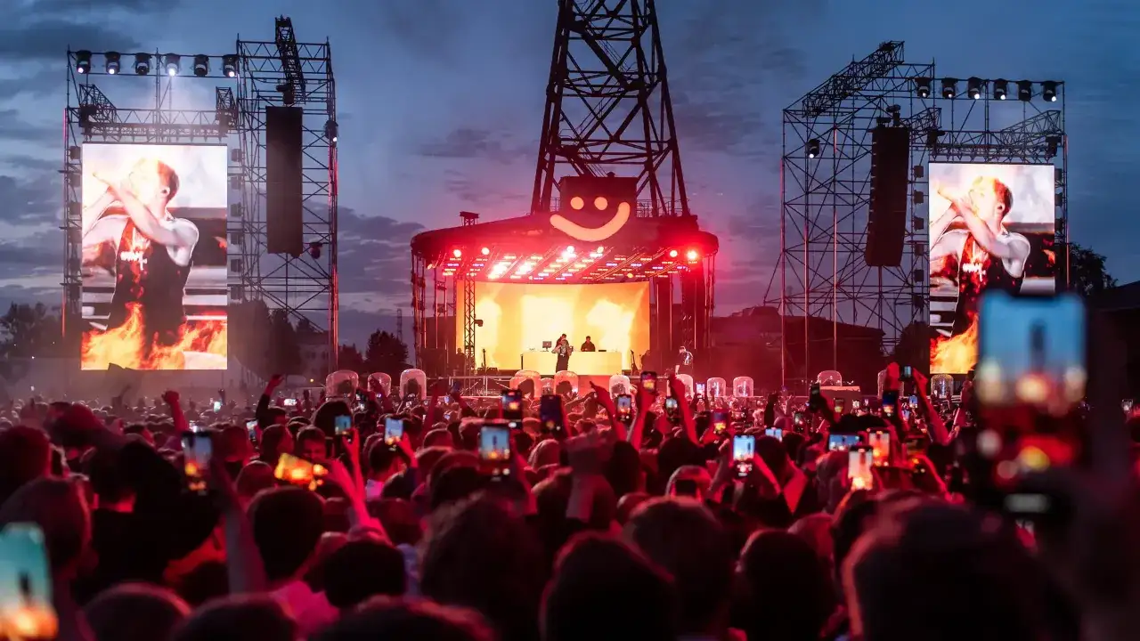 Tłum ludzi na koncercie rapera Maty, wszyscy nagrywają telefonami. W tle scena z wielkimi ekranami, na kt&oacute;rych widać artystę. Koncert trwa, a atmosfera jest gorąca.
