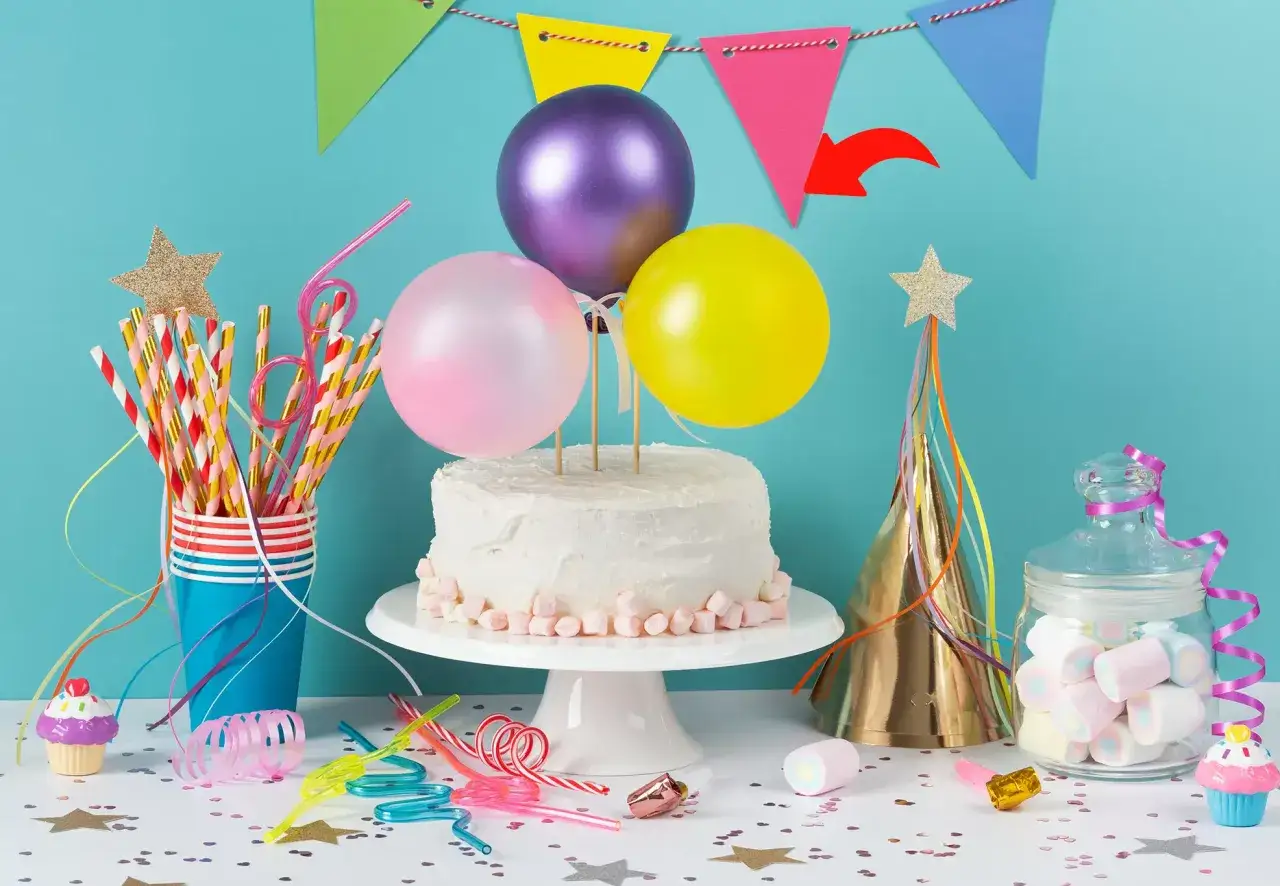Ideas para como hacer una mesa de chuches para cumpleaños: pastel blanco, globos, pajitas, gorro de fiesta y dulces.