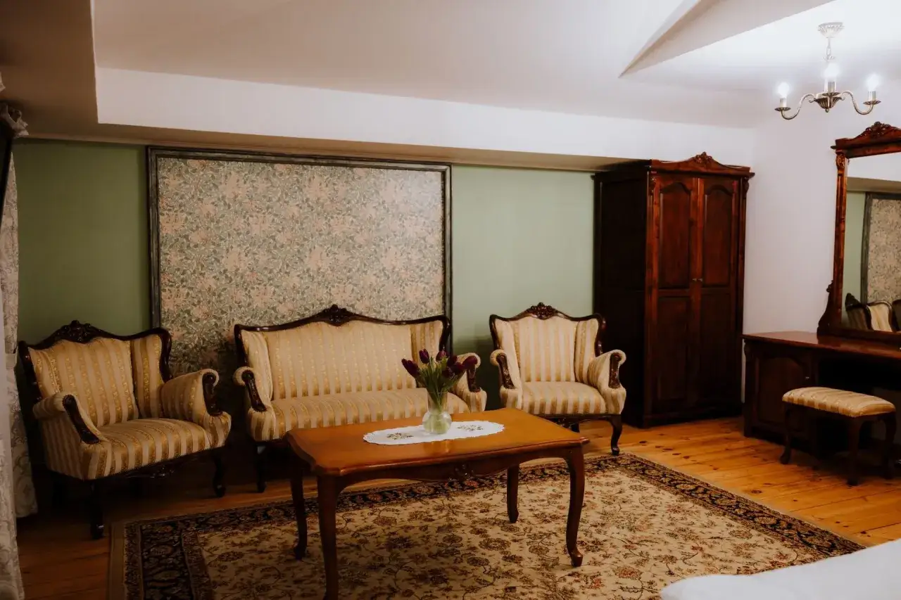 Elegancki salon w lisewskim dworze, z kanapą, fotelami, stolikiem kawowym i zabytkową szafą.