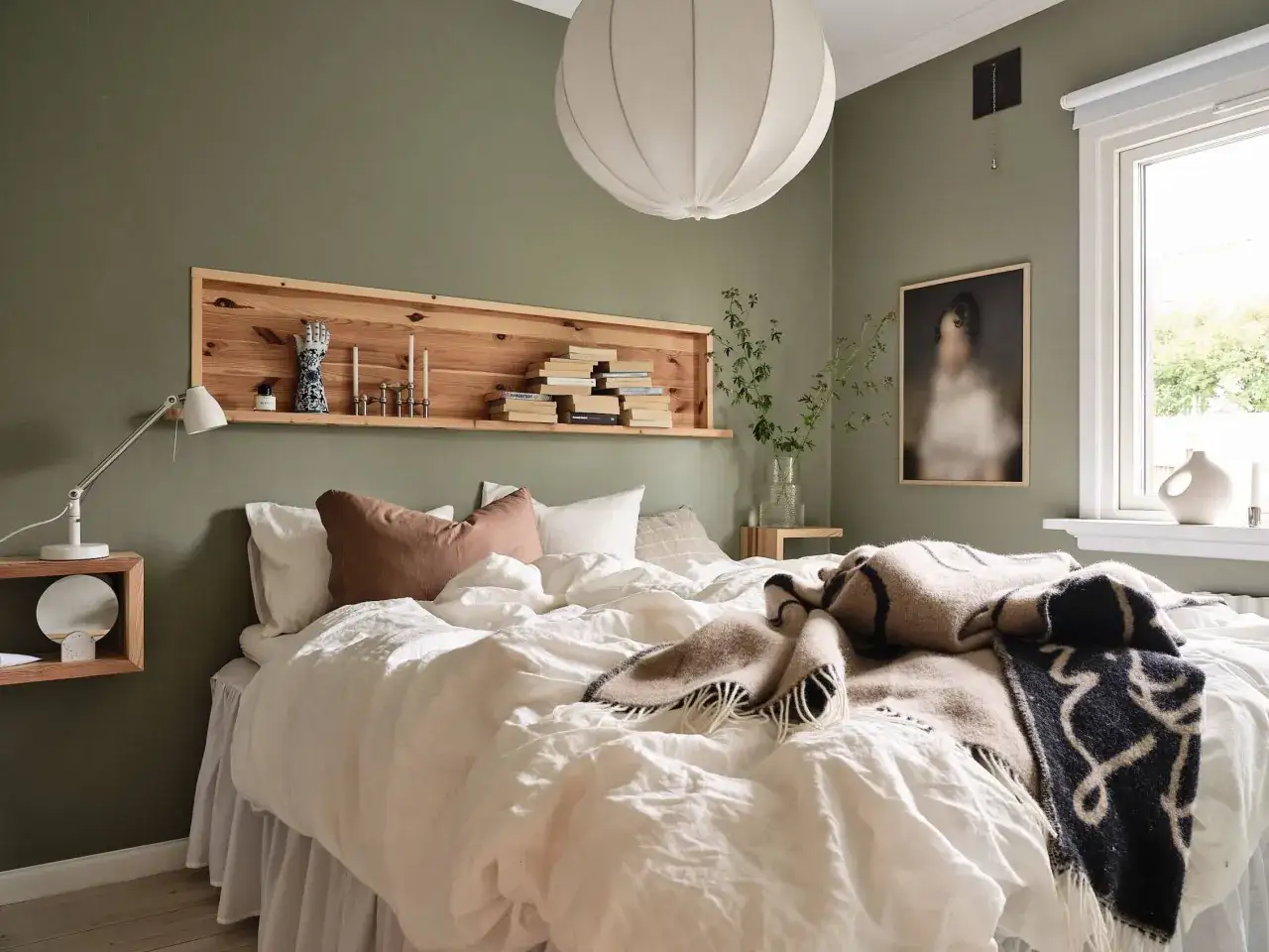 Acogedora habitación con una estantería encima de la cama, llena de libros y objetos decorativos. La cama está vestida con ropa de cama blanca y mantas cálidas.
