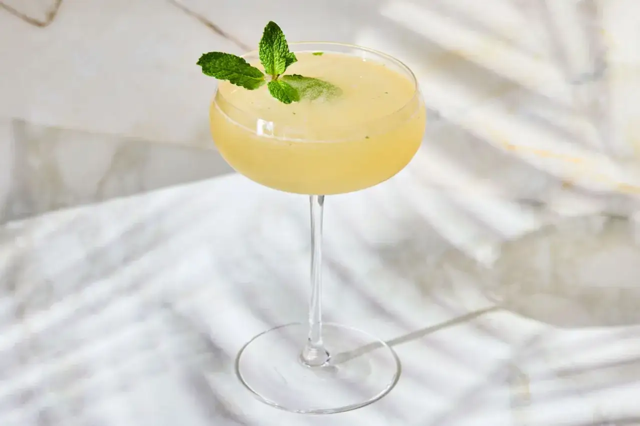 Ein erfrischender Cocktail, der an einen old cuban erinnert, mit Minze garniert, auf Marmor serviert.