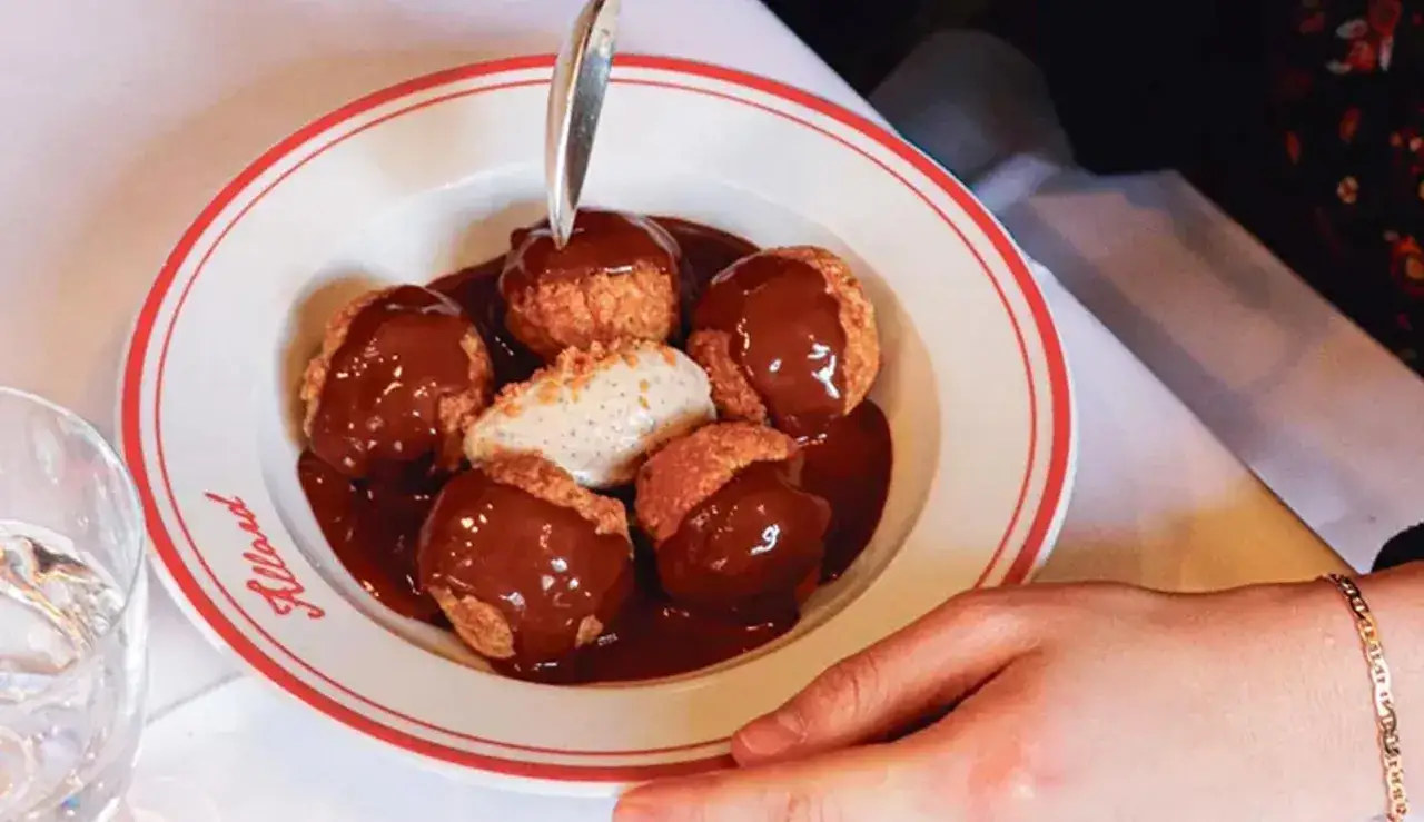Un plat de profiteroles gastronomique, nappés de chocolat chaud, avec une quenelle de glace à la vanille. Une cuillère est prête à déguster ce délice.