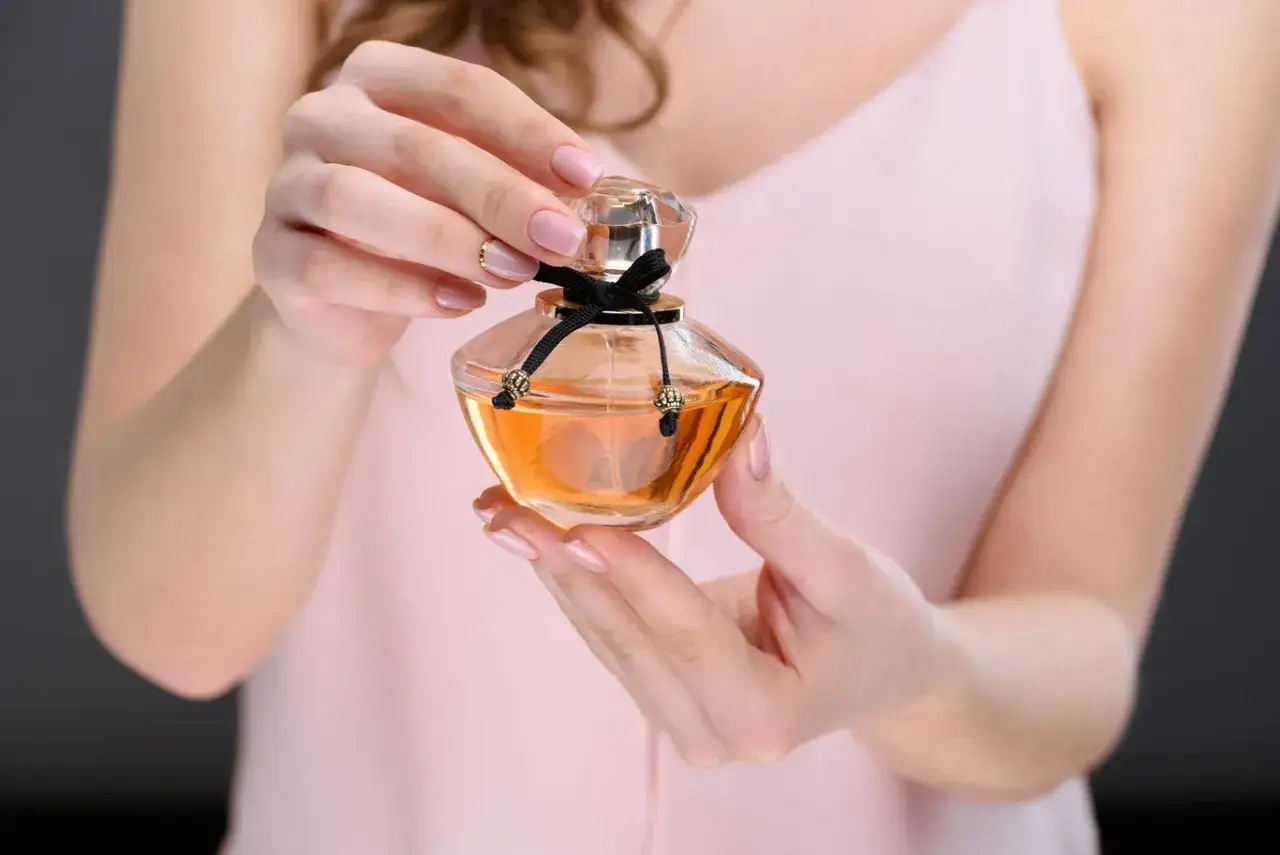 Delikatne dłonie trzymają flakonik z bursztynowym płynem. To moje ulubione perfumy, które dodają mi pewności siebie.