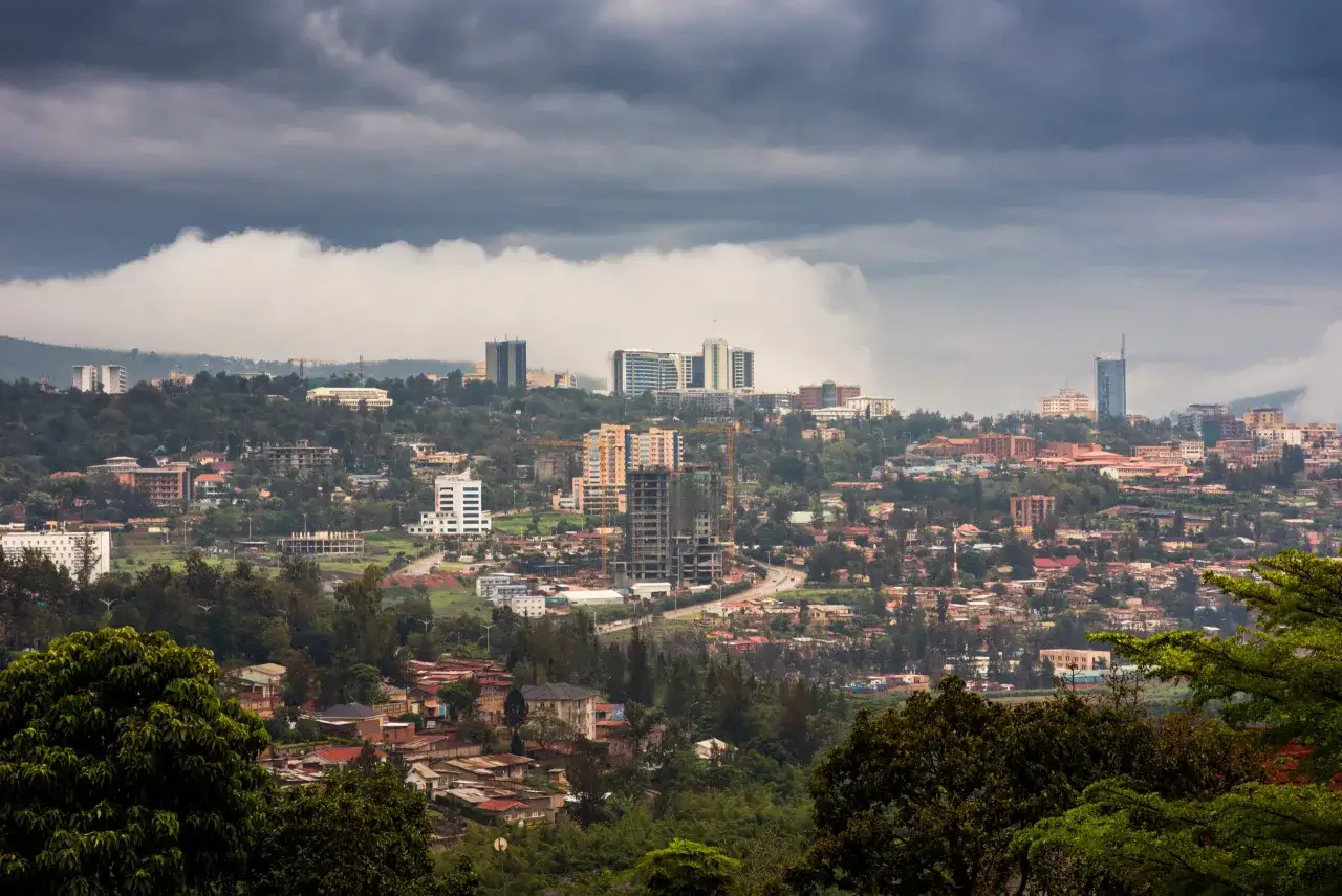 Rozległy krajobraz z Kigali, z nowoczesnymi budynkami i zielonymi wzg&oacute;rzami pod burzowymi chmurami.