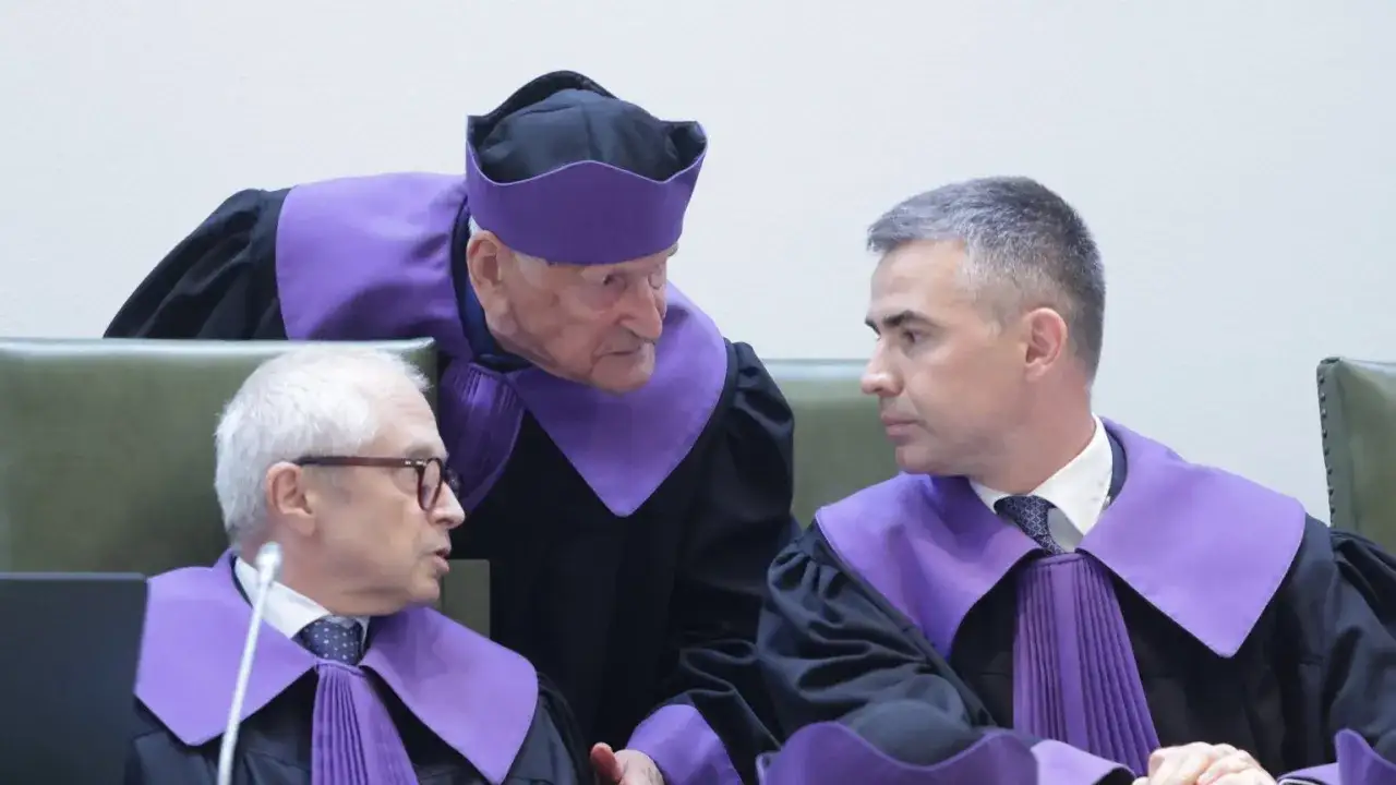 Trzech sędziów w togach dyskutuje. Starszy sędzia pochyla się nad młodszym, jakby wyjaśniał, co to impeachment.