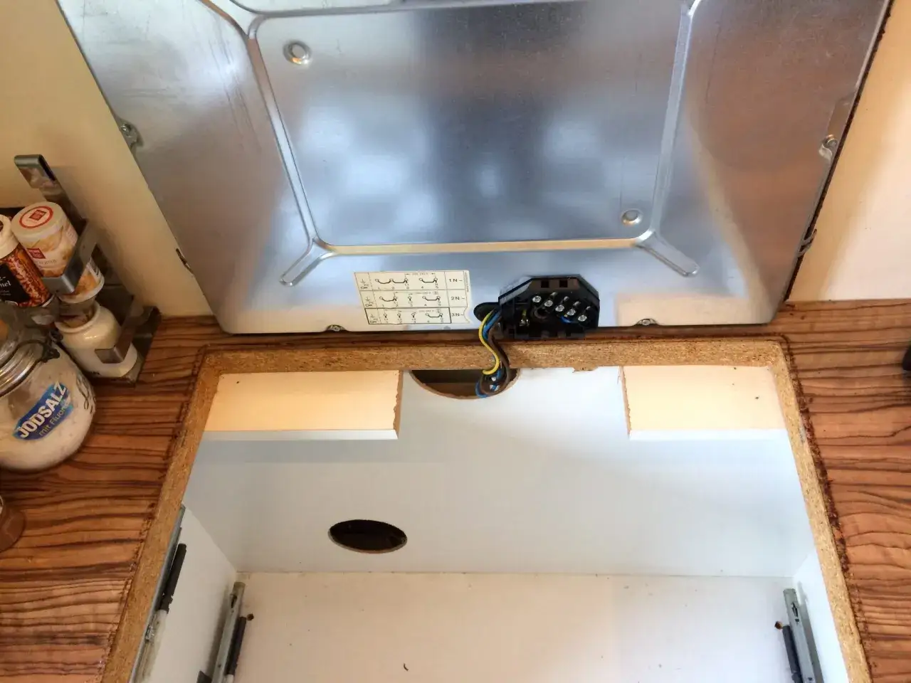 Beim Kochfeld ausbauen wird die elektrische Verbindung gel&ouml;st. Das Kochfeld ist angehoben, Kabel und Anschlussklemme sichtbar.
