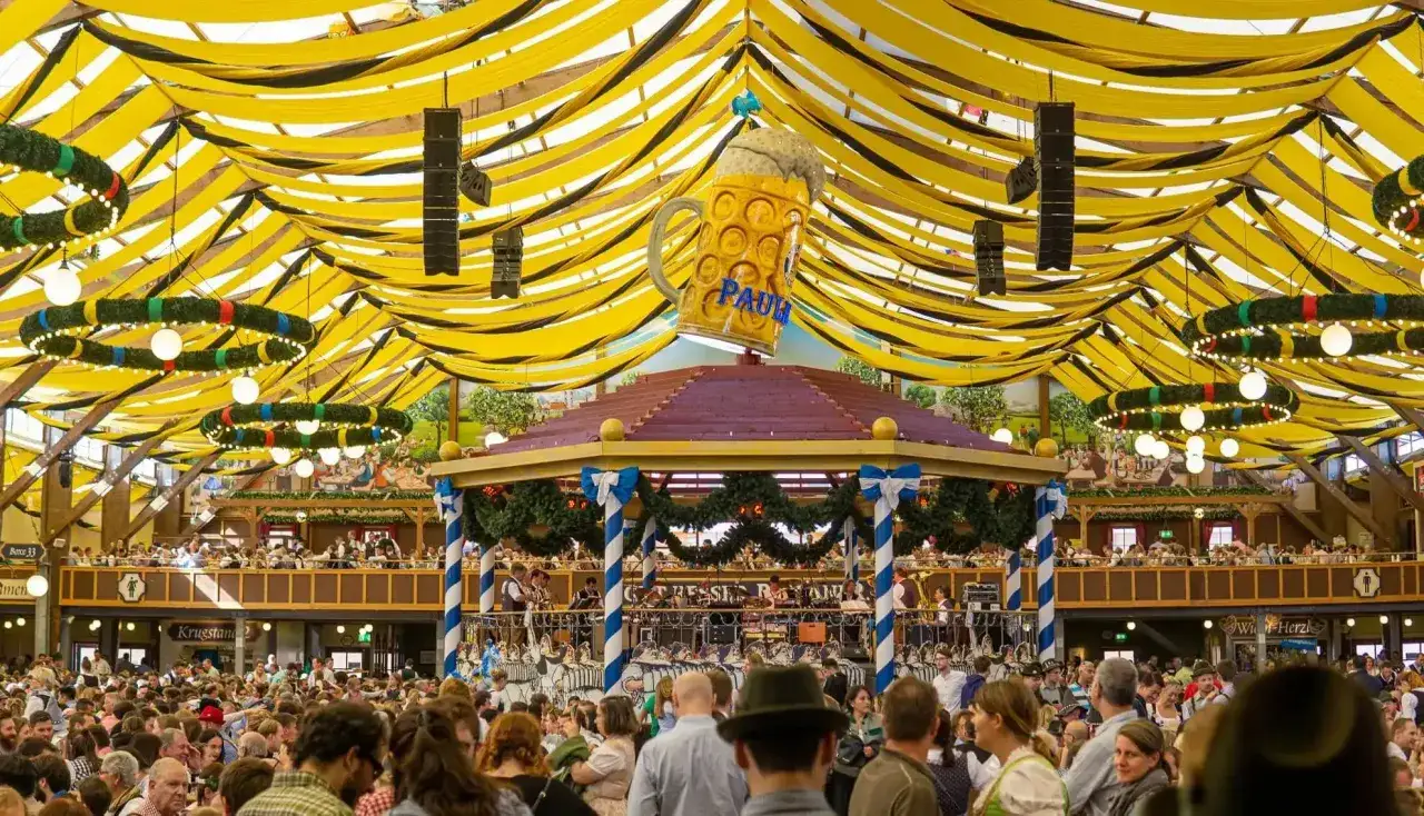 Festa a Monaco, un'enorme birra gigante domina il tendone giallo e nero dell'Oktoberfest. La folla festeggia sotto le decorazioni.