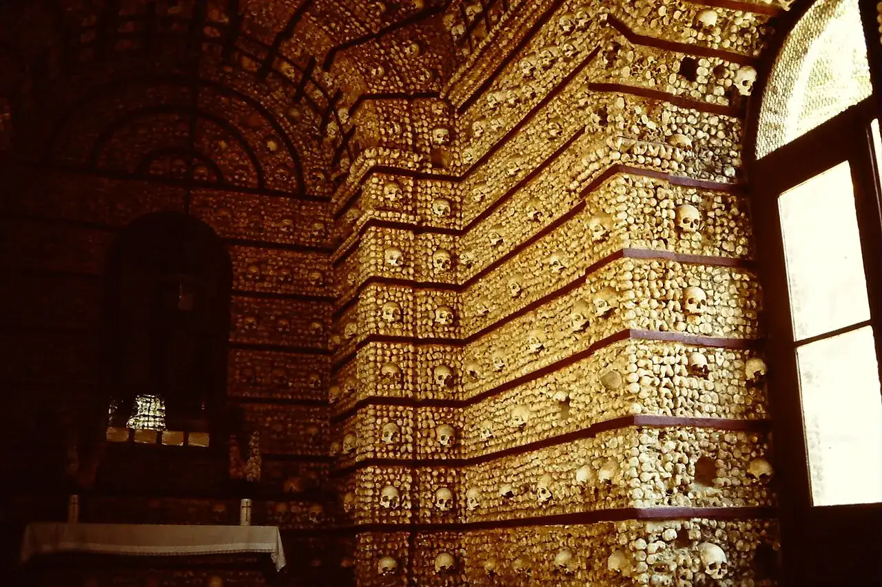 Die Capela dos Ossos, eine Kapelle, deren Wände und Decken mit menschlichen Knochen und Schädeln bedeckt sind. Ein Fenster wirft Licht auf die makabre Dekoration.