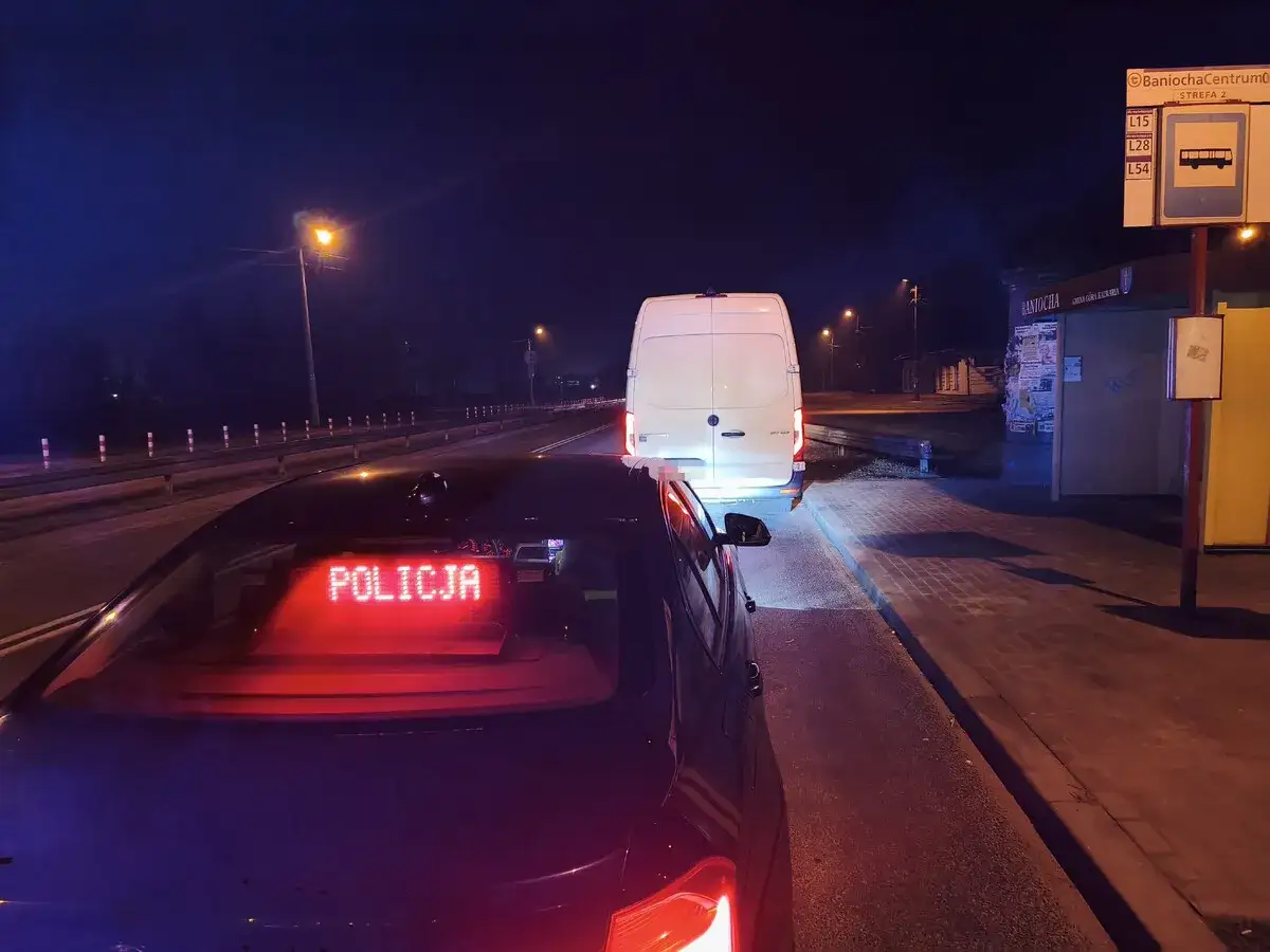 Nocna akcja policji. Biały bus zatrzymany, prawdopodobnie za przekroczenie prędkości o 50 km/h. Na dachu radiowozu świeci napis 