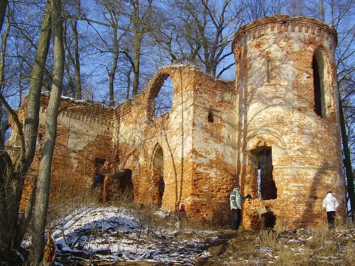Ruiny zamku, które wyglądają jak straszne miejsca, otoczone drzewami. Widać ludzi zwiedzających to opuszczone miejsce.