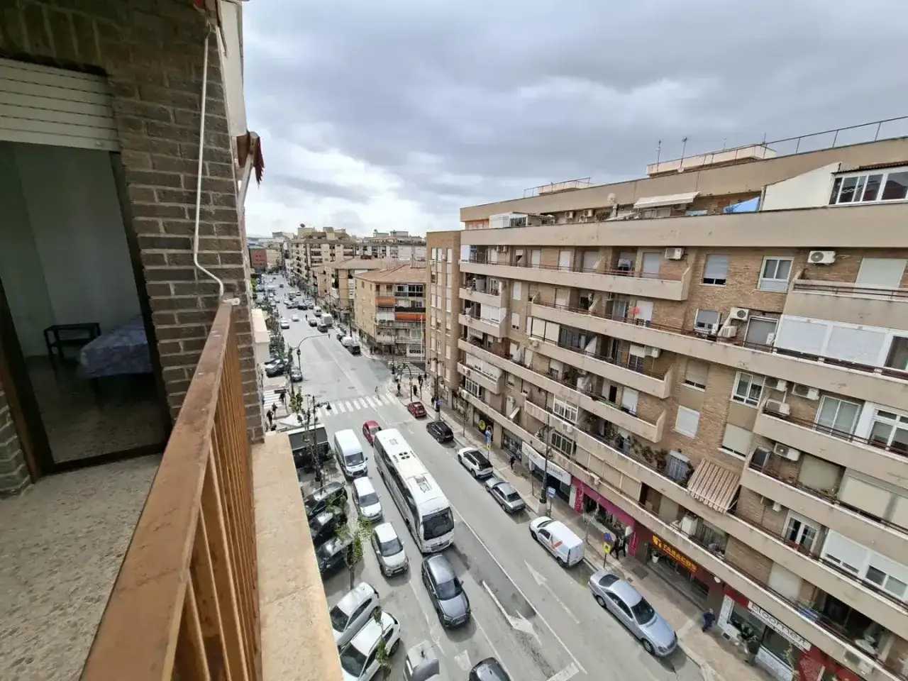 Vista aérea de una calle urbana con edificios residenciales y comerciales. Un autobús y varios coches circulan por la carretera. Ideal para haya real estate.