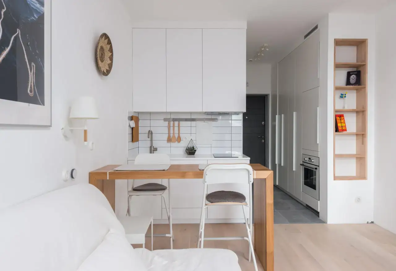 Cocina y sala de estar de una tiny house moderna. Muebles blancos, encimera de madera y suelo de parquet.