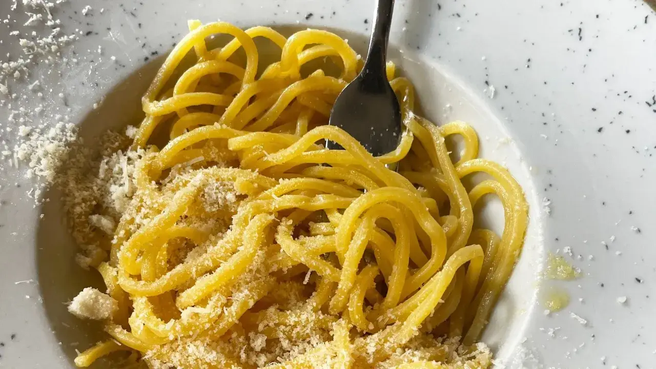 Un piatto di pasta in bianco, spaghetti conditi con olio e abbondante parmigiano grattugiato, pronti per essere gustati.