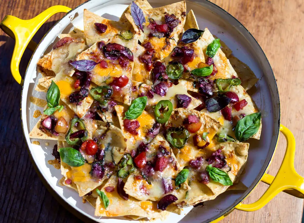 Ein köstlicher **nacho salat** mit geschmolzenem Käse, Jalapeños, Oliven und frischem Basilikum, serviert in einer gelben Pfanne.