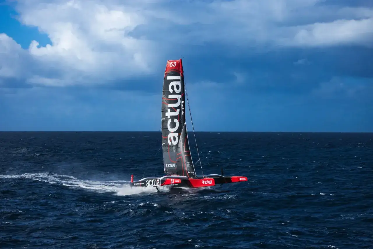 Le trimaran Sodebo Ultim 3 fend les vagues, sa voile noire et rouge #actual portant le numéro 53, prêt pour la prochaine aventure.