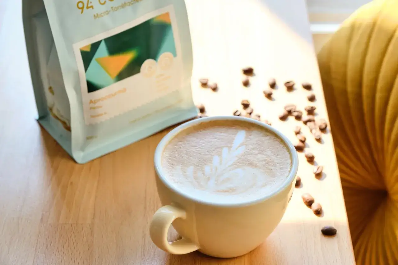En krämig iskaffe med lattekonst, bredvid en påse kaffebönor. Perfekt för ett hemmagjort iskaffe recept.