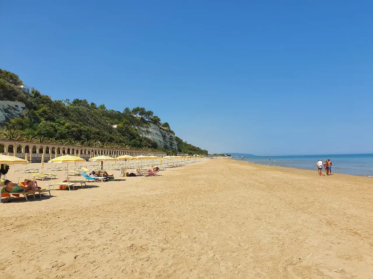Spiaggia di ponente Rodi Garganico: sabbia dorata, ombrelloni gialli e un mare azzurro sotto un cielo limpido.