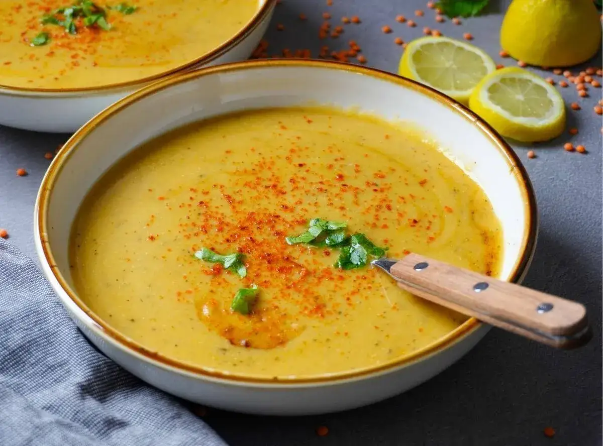 Eine dampfende Sch&uuml;ssel Mercimek Corbasi, garniert mit Kr&auml;utern und Paprikapulver, daneben Zitronenspalten.