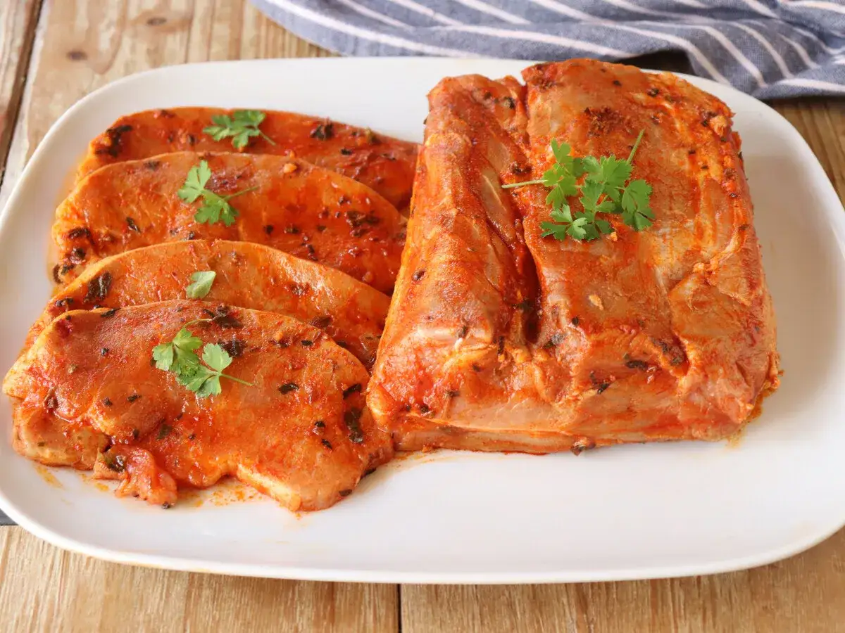 Un trozo de lomo adobado y filetes listos para cocinar, decorados con perejil fresco.