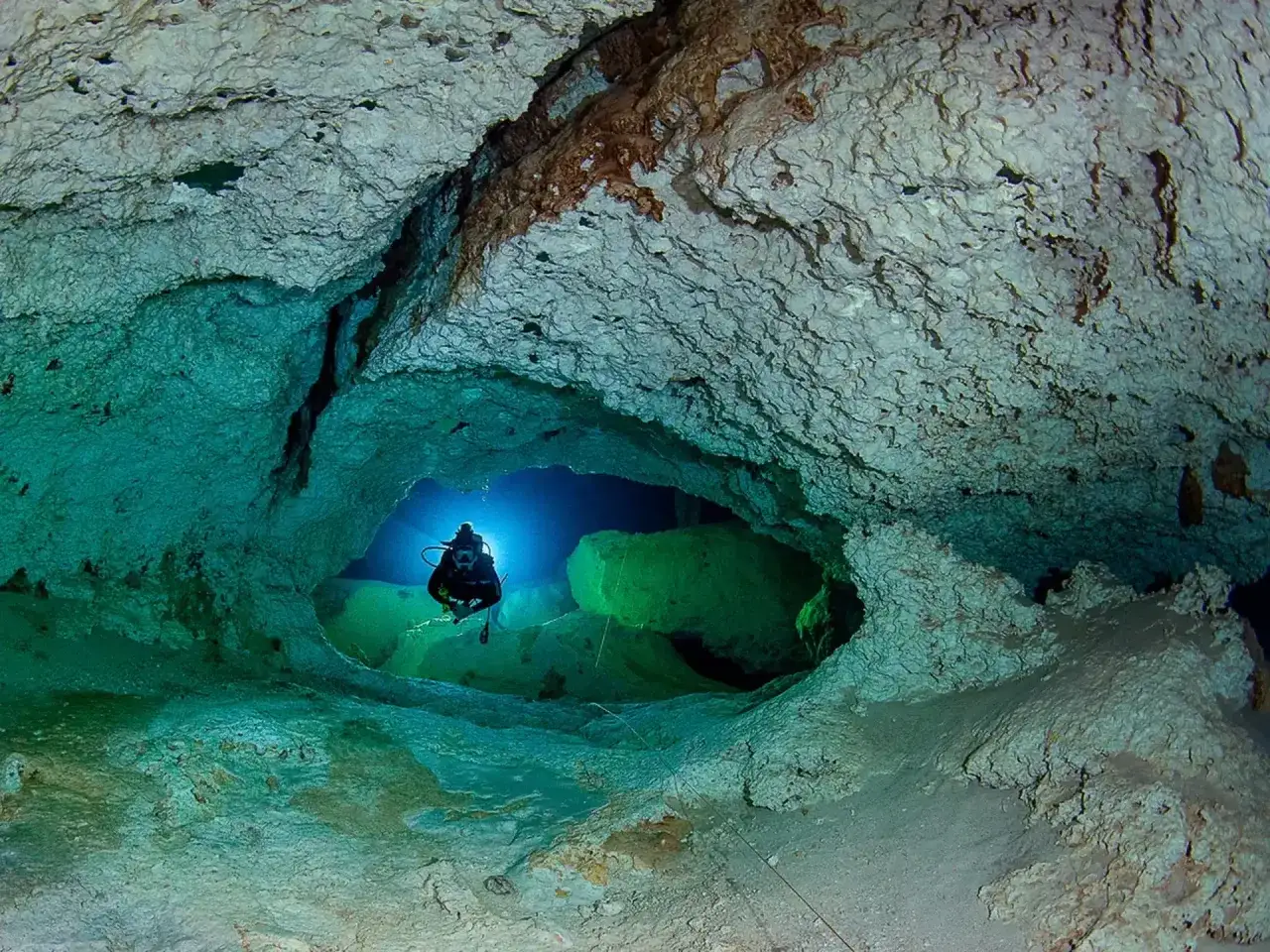 Buceador explorando la asombrosa profundidad de un cenote, rodeado de formaciones rocosas y aguas turquesas.