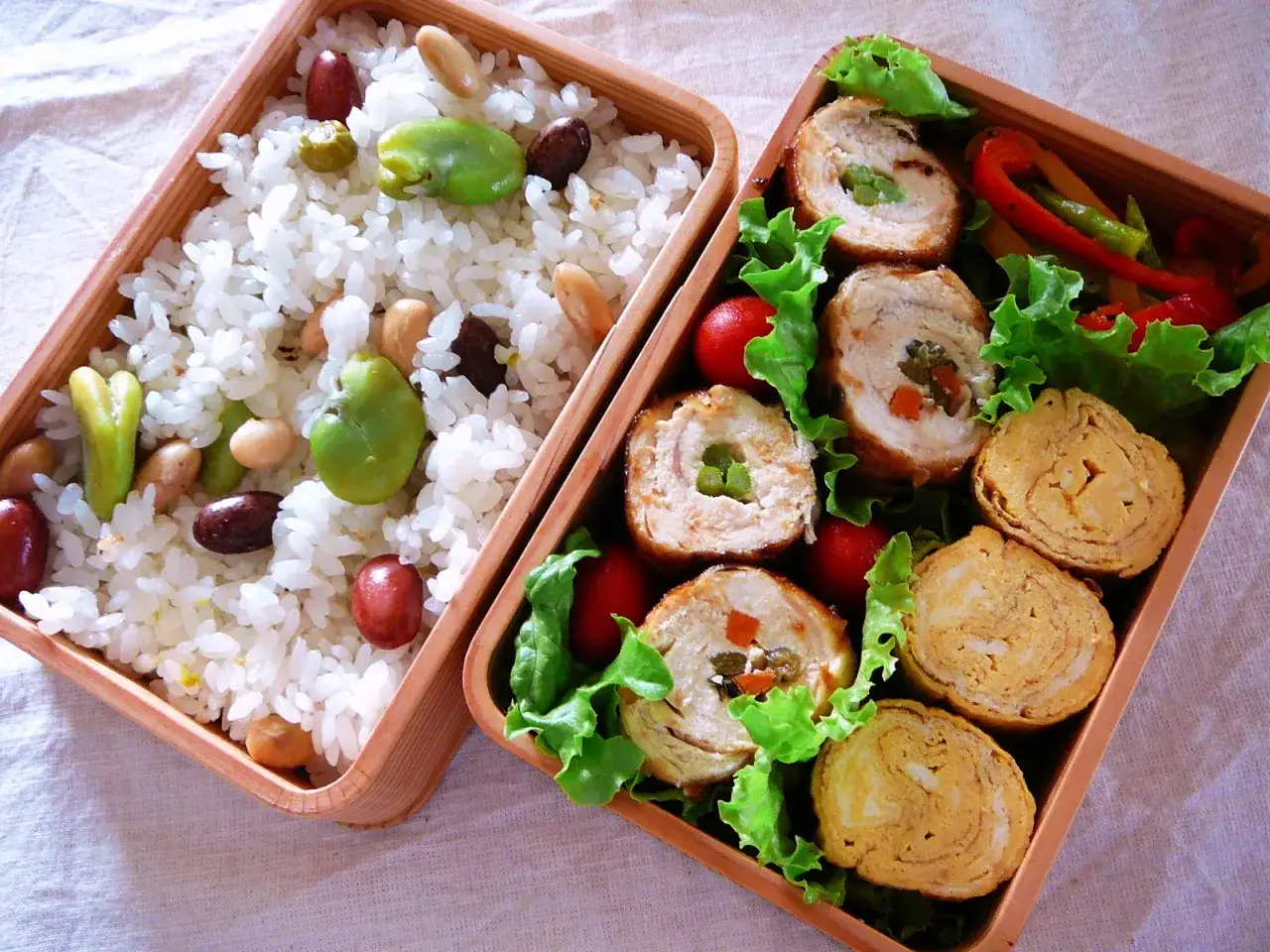 A bento box with rice, beans, chicken rolls, and tamagoyaki (rolled omelet).