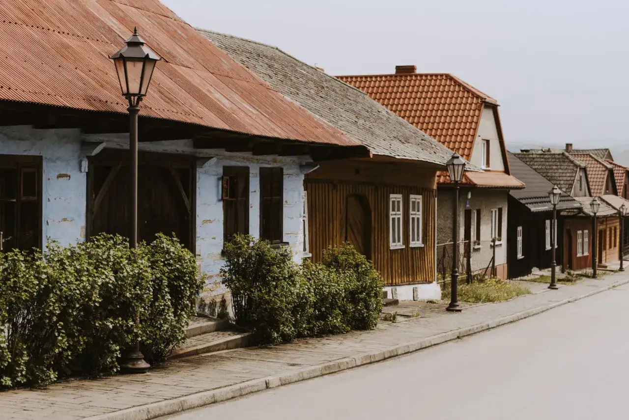 Urokliwa wieś w Polsce z rzędem domów o tradycyjnej architekturze, brukowanym chodnikiem i zabytkowymi latarniami.