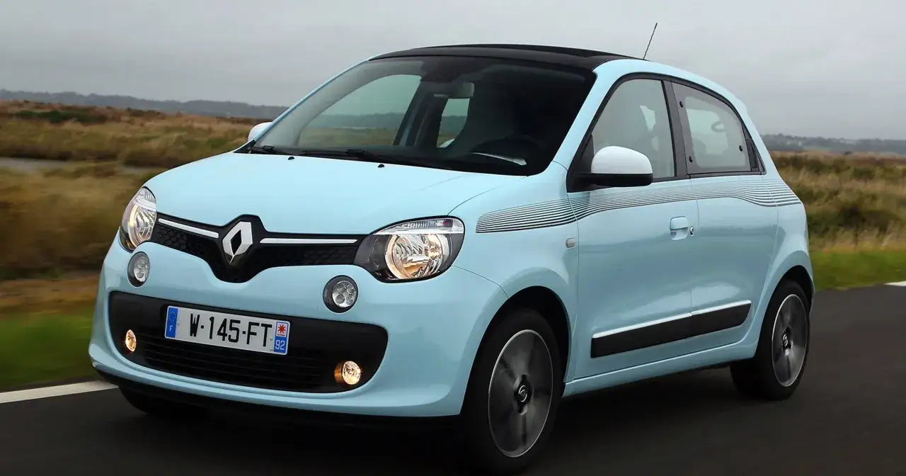 Jasnoniebieskie renault twingo 3 z czarnym dachem i ozdobnymi pasami pędzi po drodze wśród traw.
