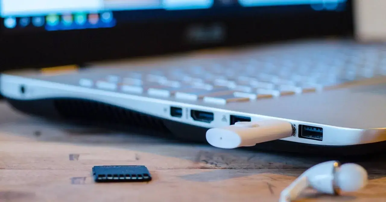 Biały pendrive podłączony do laptopa, obok karta pamięci i słuchawki. Prosty sposób, jak otworzyć pendrive na laptopie.